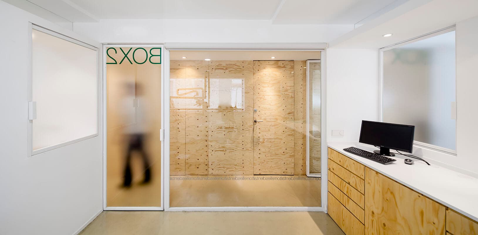 Vista desde el interior de uno de los boxes. Se juega con elementos de vidrio translúcido y transparente y con mobiliario y revestimientos de madera de pino.